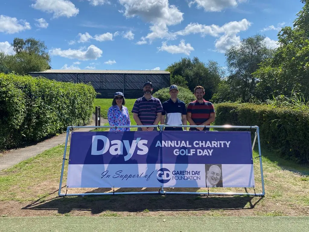 3 Men and 1 woman stood in front of Day's Annual Charity Golf Day banner