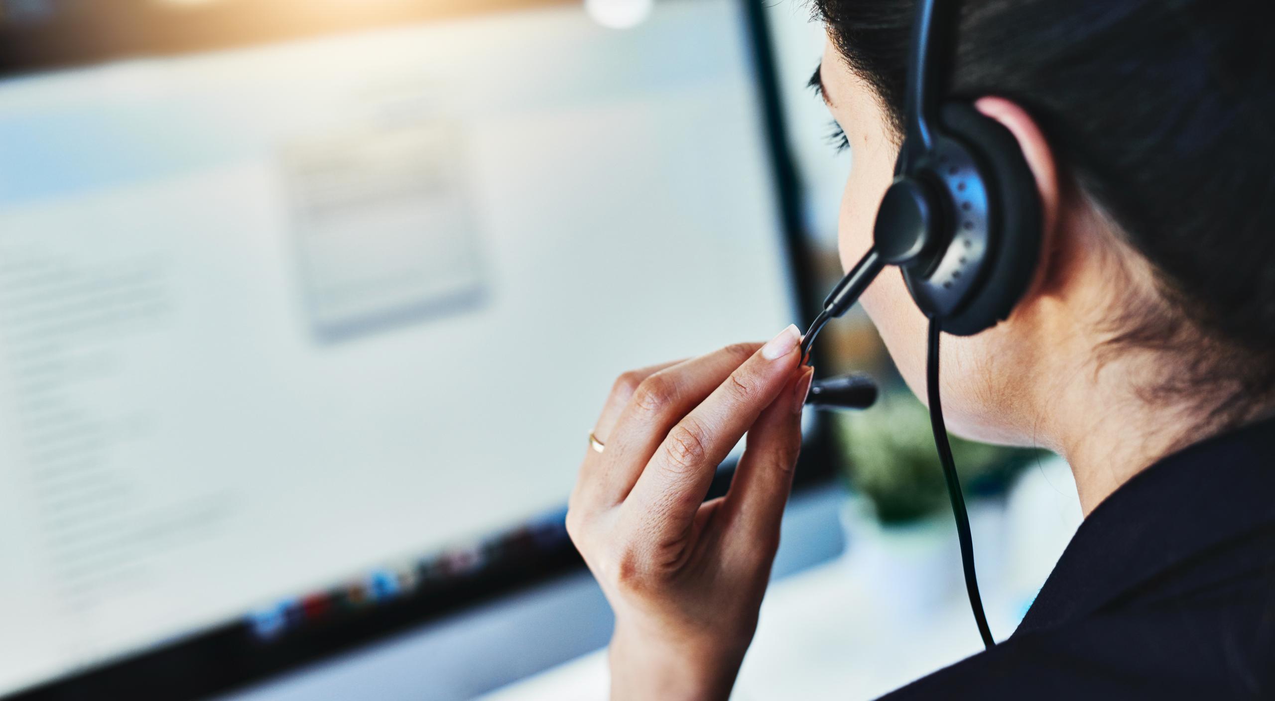 A woman wearing a headset, looking at a computer screen