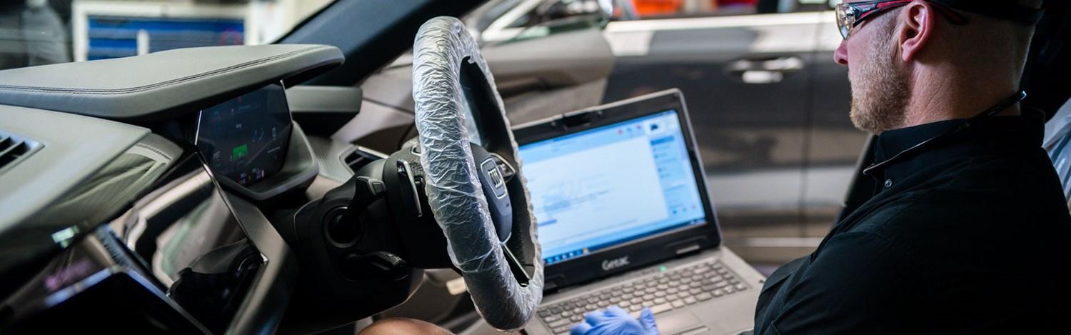 Audi Repair Specialist makes notes on laptop while sitting in the inside of an Audi vehicle during repair at Belfast Audi