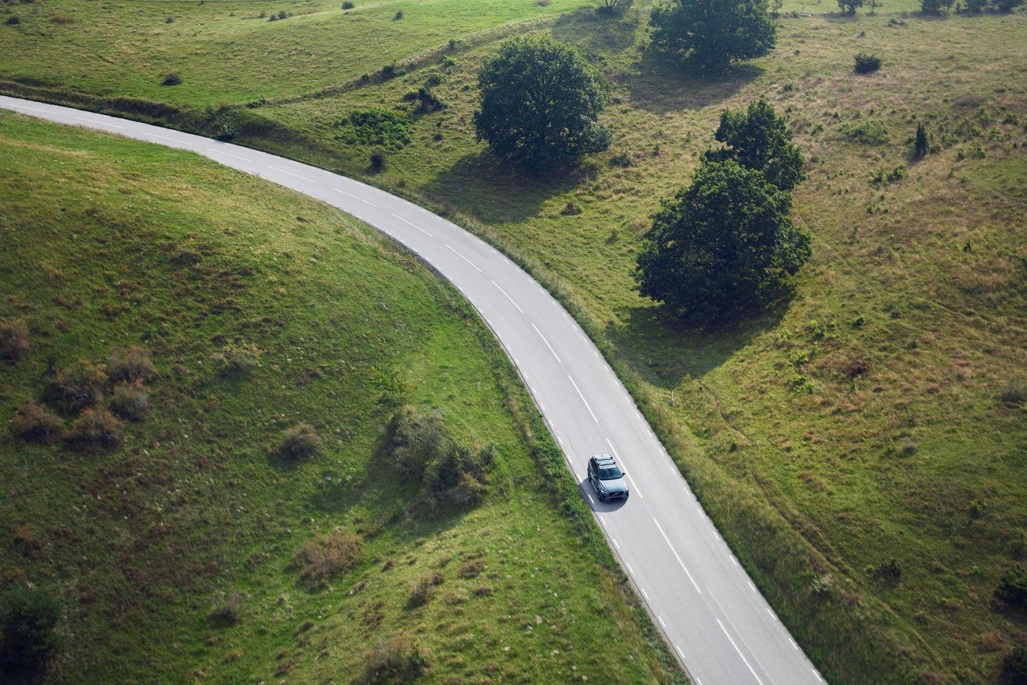New grey Volvo car drives along winding countryside road