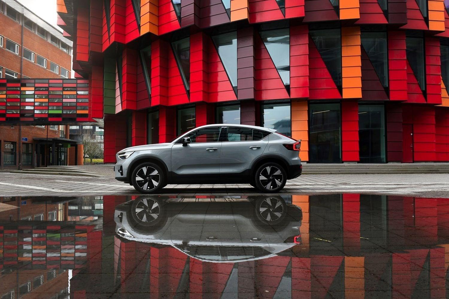 Side view of the all-new Volvo C40 Recharge in silver, parked on street with circular multicoloured tiled building behind