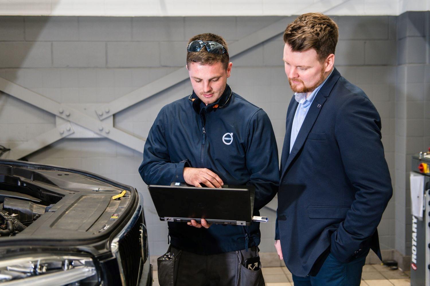 Volvo Repair Specialist inspects used car on laptop with Volvo customer in Volvo Repair Centre for electrical repairs