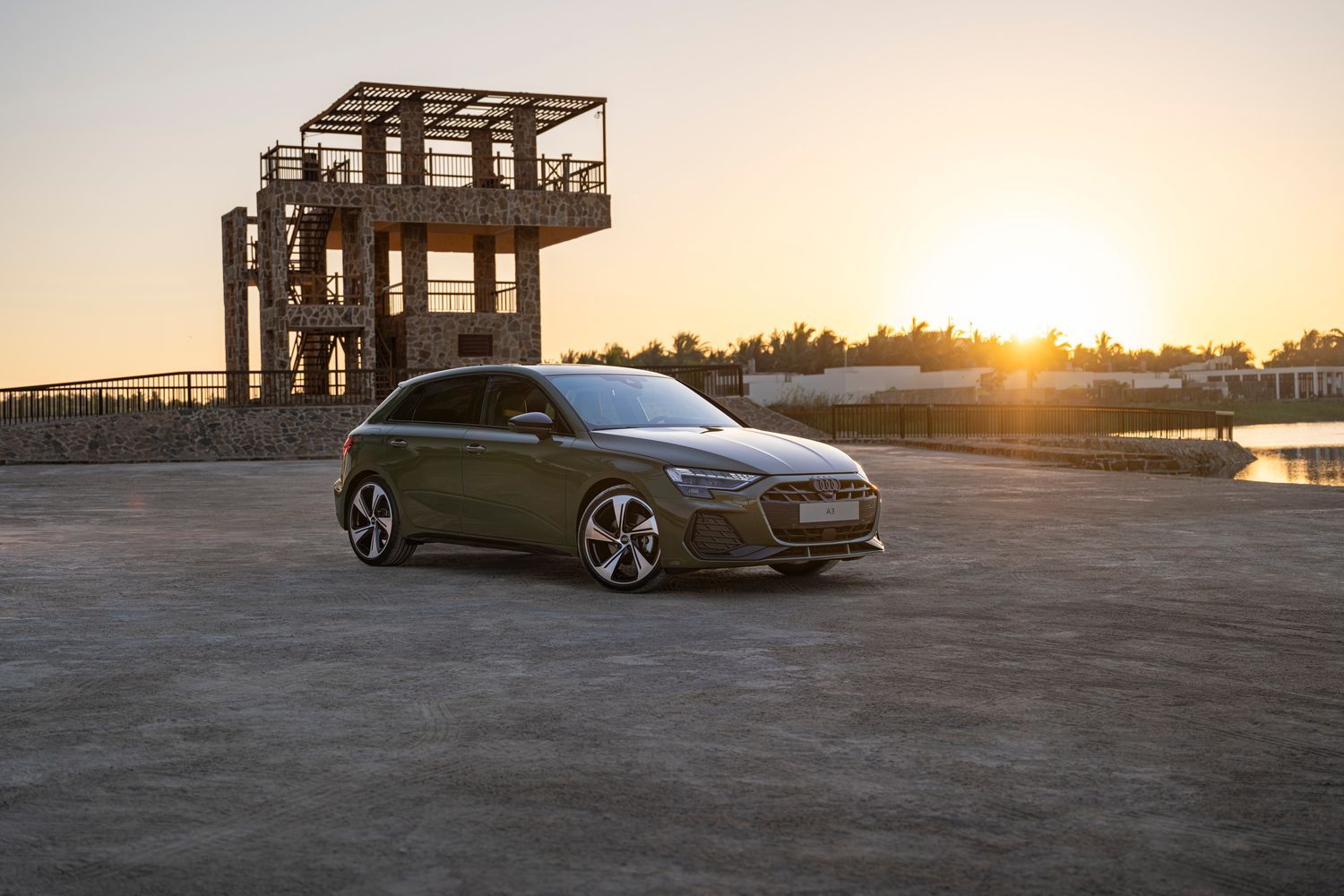 New Audi A3 Sportback (2024) in grey, parked in car park with the sun setting behind. The vehicle is parked in a way to highlight the front and side features of the car.