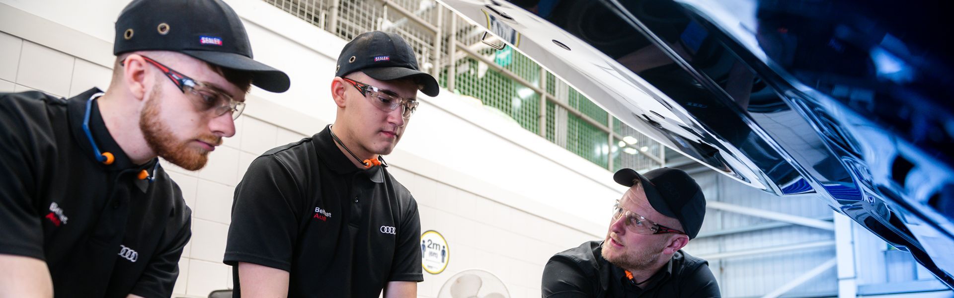 Three Audi Technicians inspect under the hood of an Audi vehicle during maintenance work at Belfast Audi