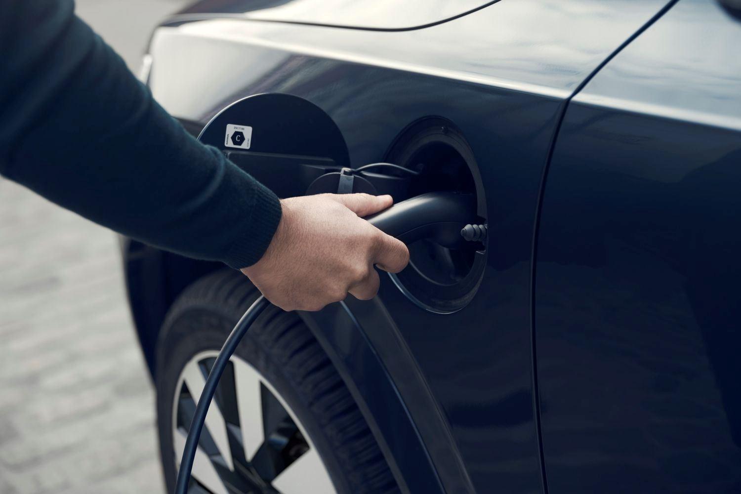 Close-up of the Volvo XC90 Recharge in black, getting charged as person plugs in charger