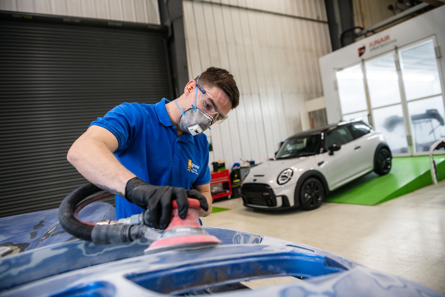 Agnew Repair Centre Specialist pre-sands the hood of a damaged vehicle for preparation for filler application.