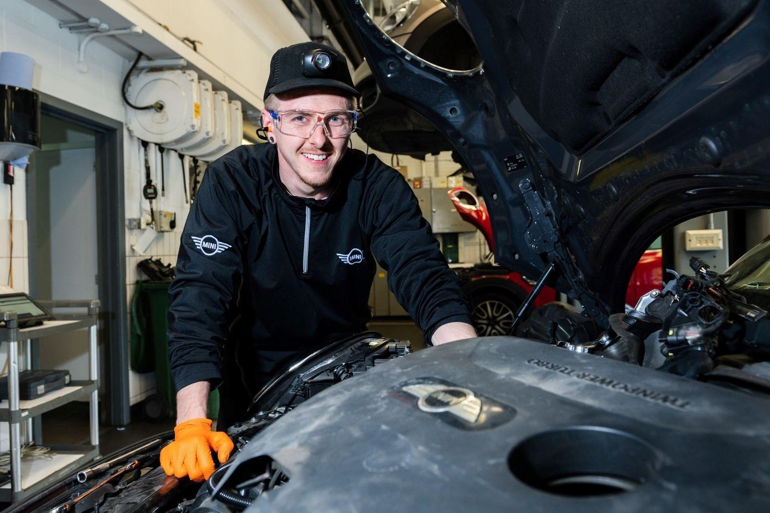 Smiling MINI Repair Specialist stands beside open hood of a MINI during a repair at the MINI Repair Centre at Bavarian MINI