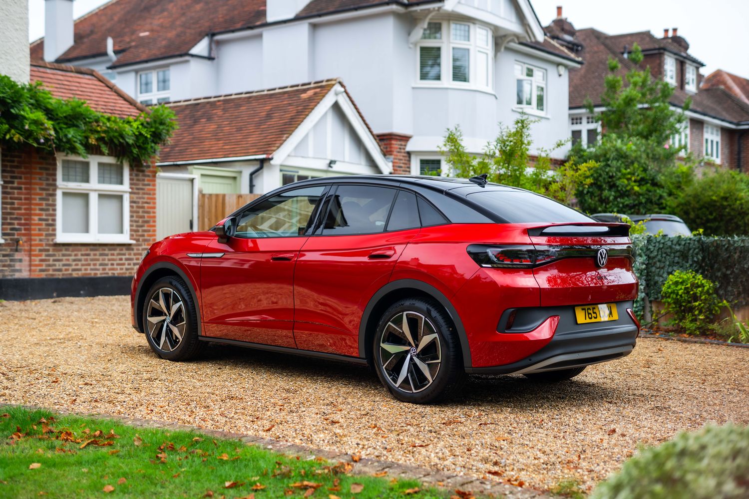 Side view of the new Volkswagen ID.5 in red, parked to the side of a house on a gravel drive