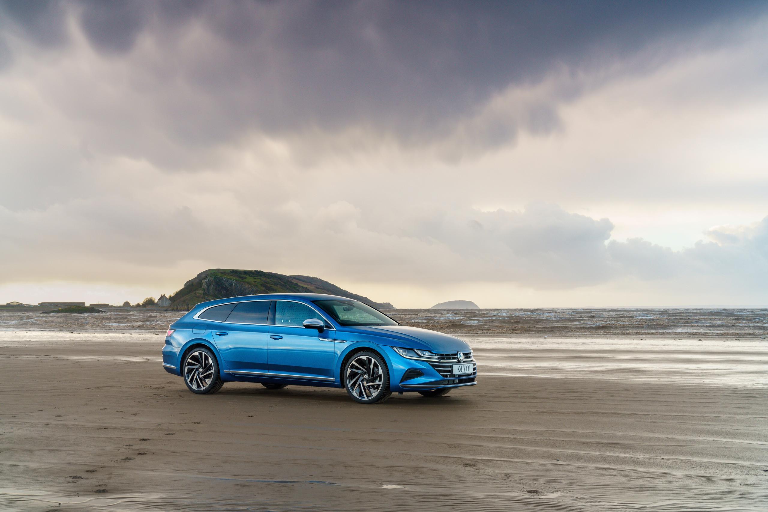 Side view of the new Volkswagen Arteon Shooting Brake in blue, parked on beach with sea behind