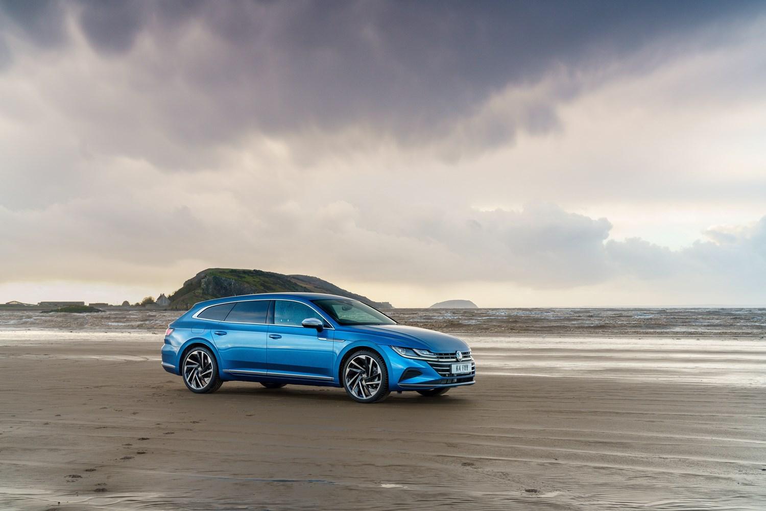 Side view of the new Volkswagen Arteon Shooting Brake in blue, parked on beach with sea behind