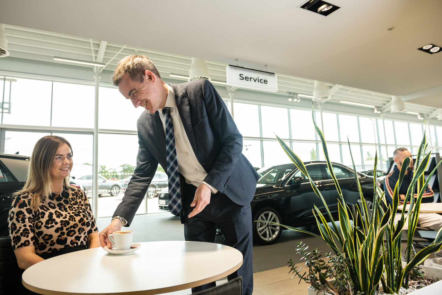 Audi Customer Service Specialist gives refreshments to customer in the Audi Showroom at Belfast Audi