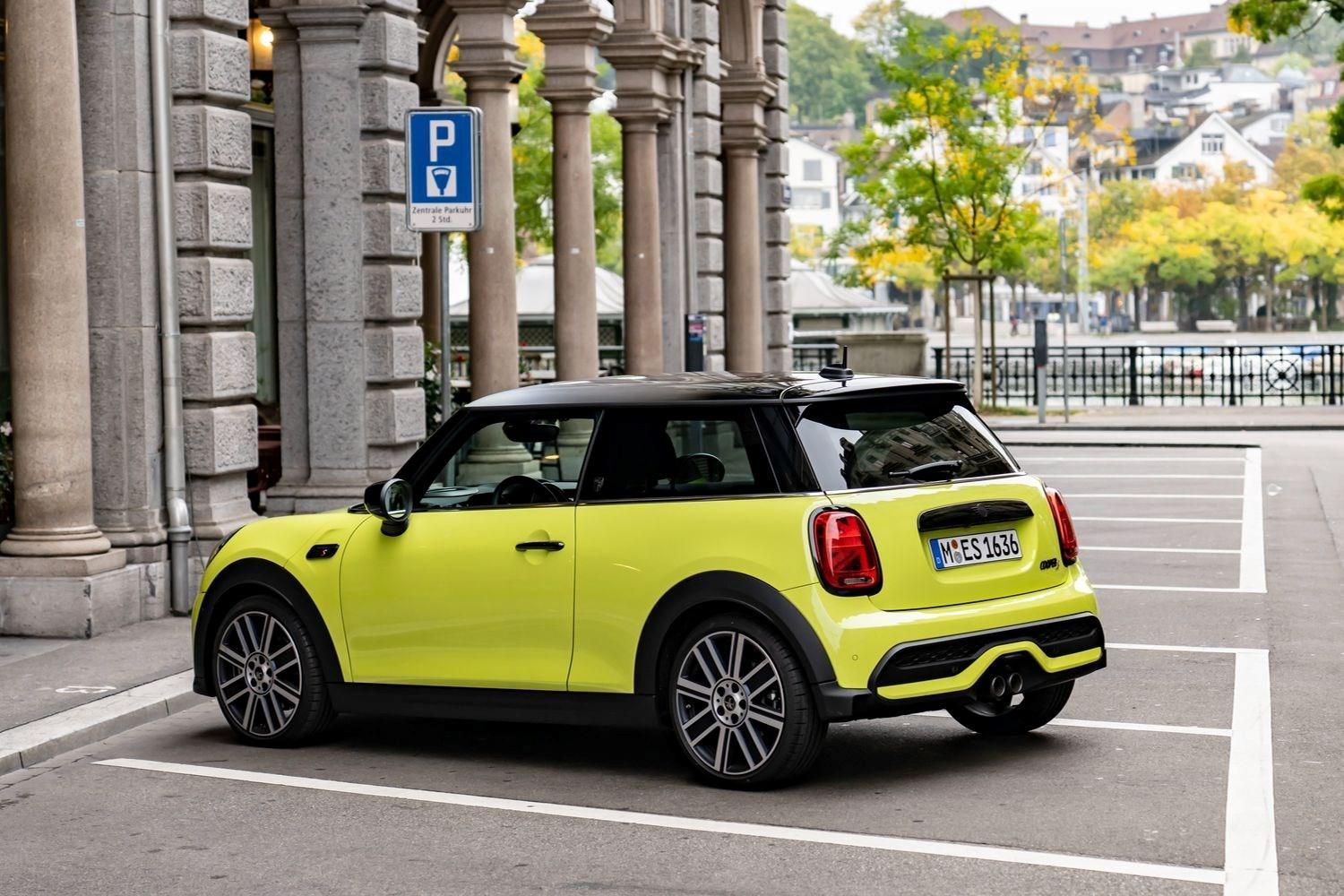 Side view of the new MINI 3-Door Hatchback in yellow, parked in car park space next to old building in European city