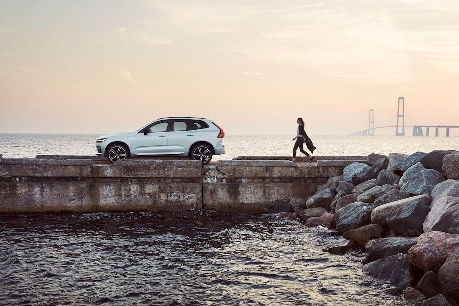 Person walks towards white Volvo XC40 that is parked on pier. River and large bridge are visible in the background.