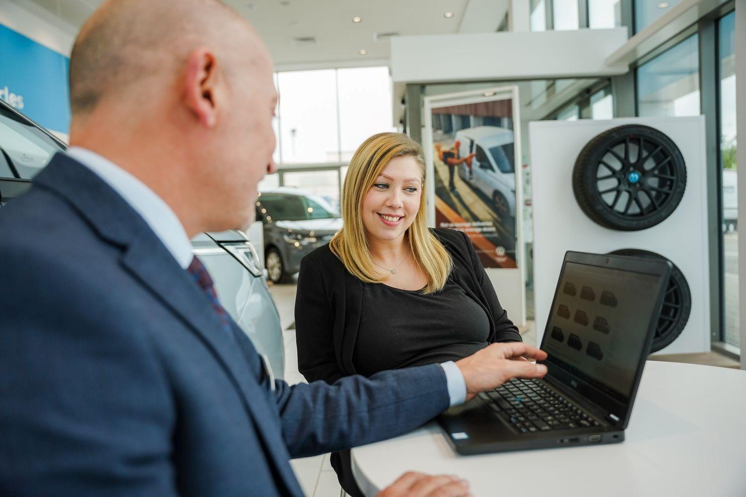 Volkswagen Sales Advisor shows warranty options to customer on laptop at the Agnew Volkswagen Belfast showroom, Belfast, Northern Ireland.