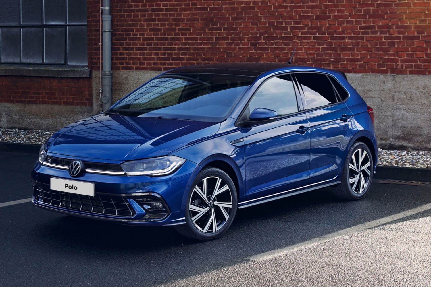 Front and side view of the new Volkswagen Polo in blue, parked in front of a red brick building