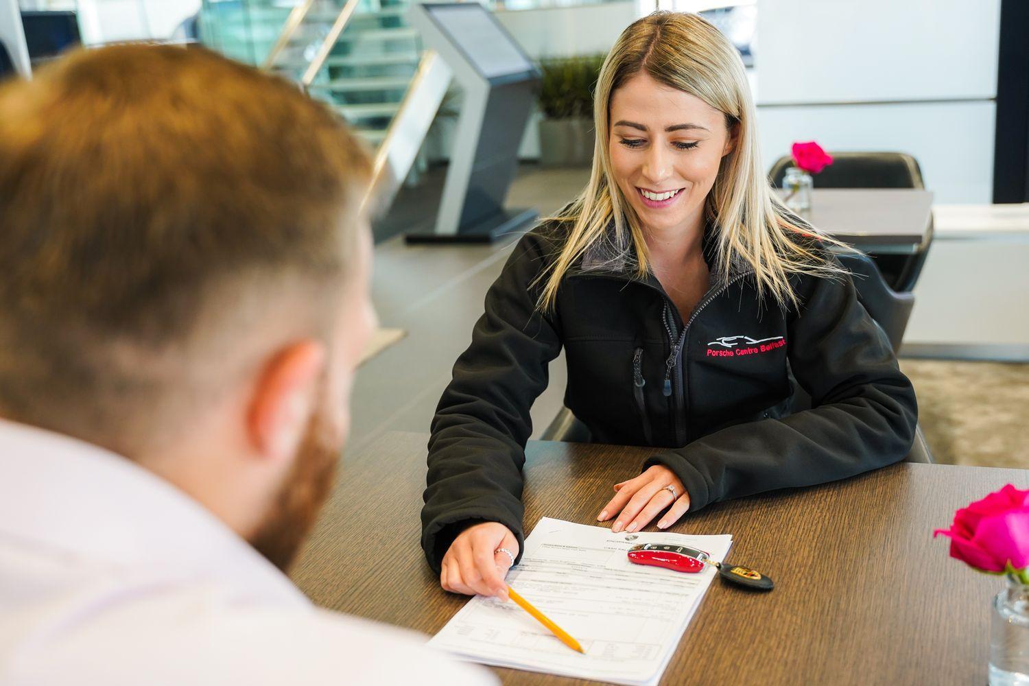 Porsche Sales Advisor sits at desk across from customer to discuss the extended warranty options available for their new Porsche Vehicle