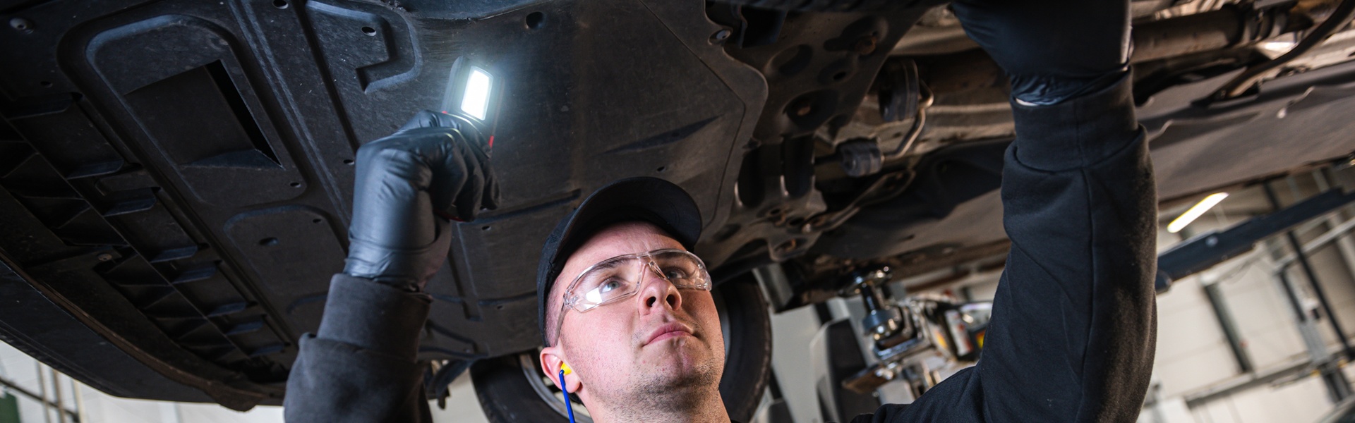 Volkswagen Service Specialist checks underneath a Volkswagen Touran with light at the Volkswagen Approved Accident Repair Centre, Agnew Volkswagen Belfast