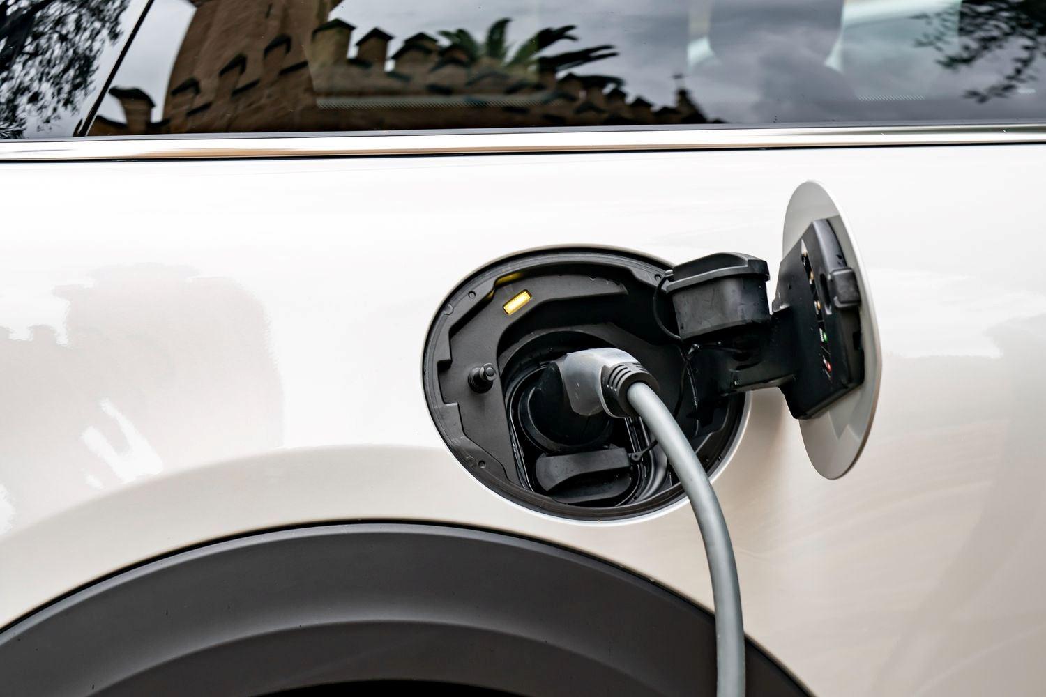 Exterior view of the new MINI Electric in white, close-up of the electric charging socket with charging cable plugged in
