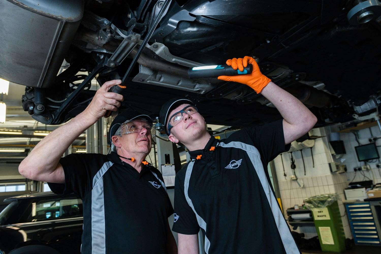 Two MINI Repair Specialists inspect the undercarriage of a MINI vehicle during routine maintenance at the MINI Repair Centre at Bavarian MINI