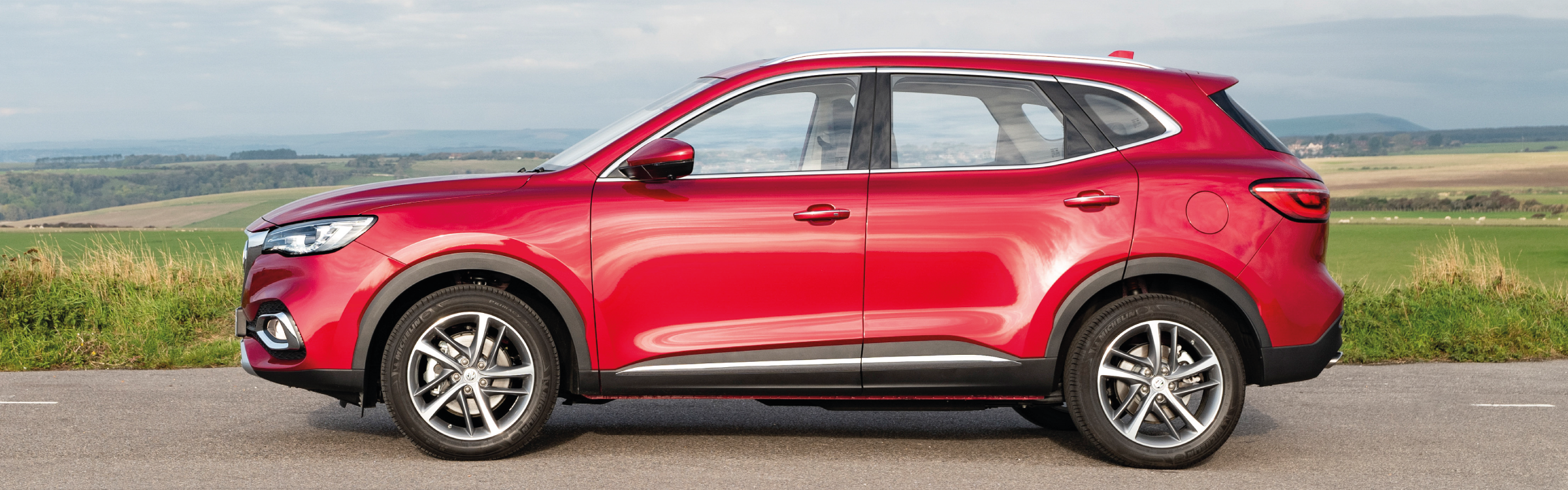 Side view of a Red MG HS plug-in parked in the countryside