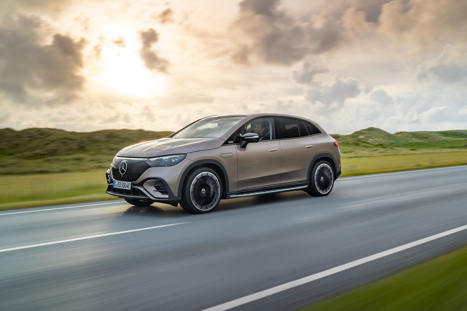 Side profile of a brown EQE SUV driving.
