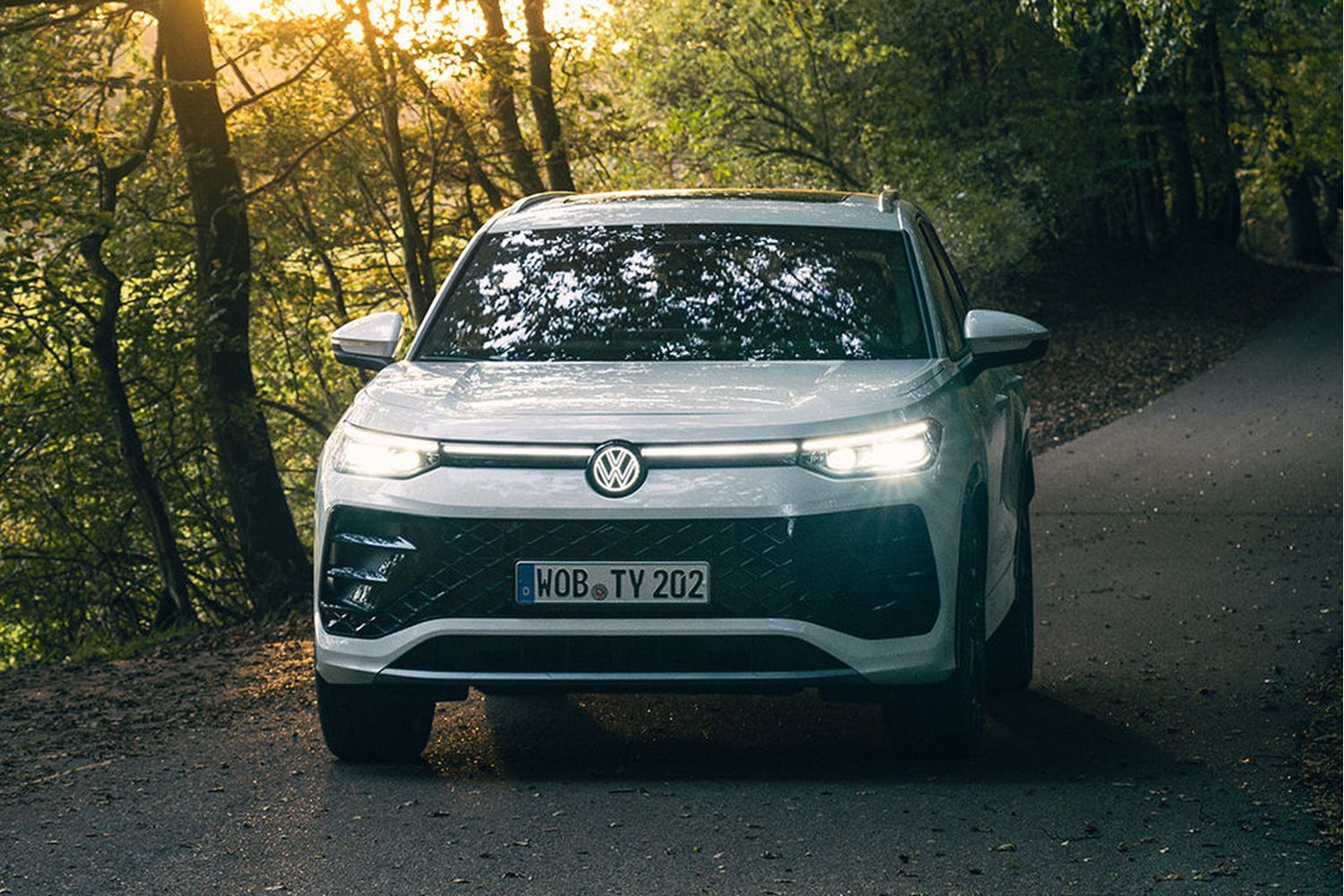 Front view of a new Volkswagen Tayron in white, driving along a road lined with trees