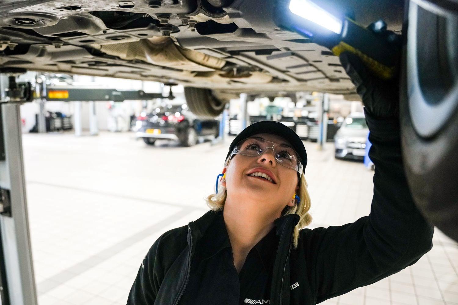 Mercedes-Benz Technician inspects the undercarriage of a Mercedes-Benz vehicle with a handheld light during MOT inspection