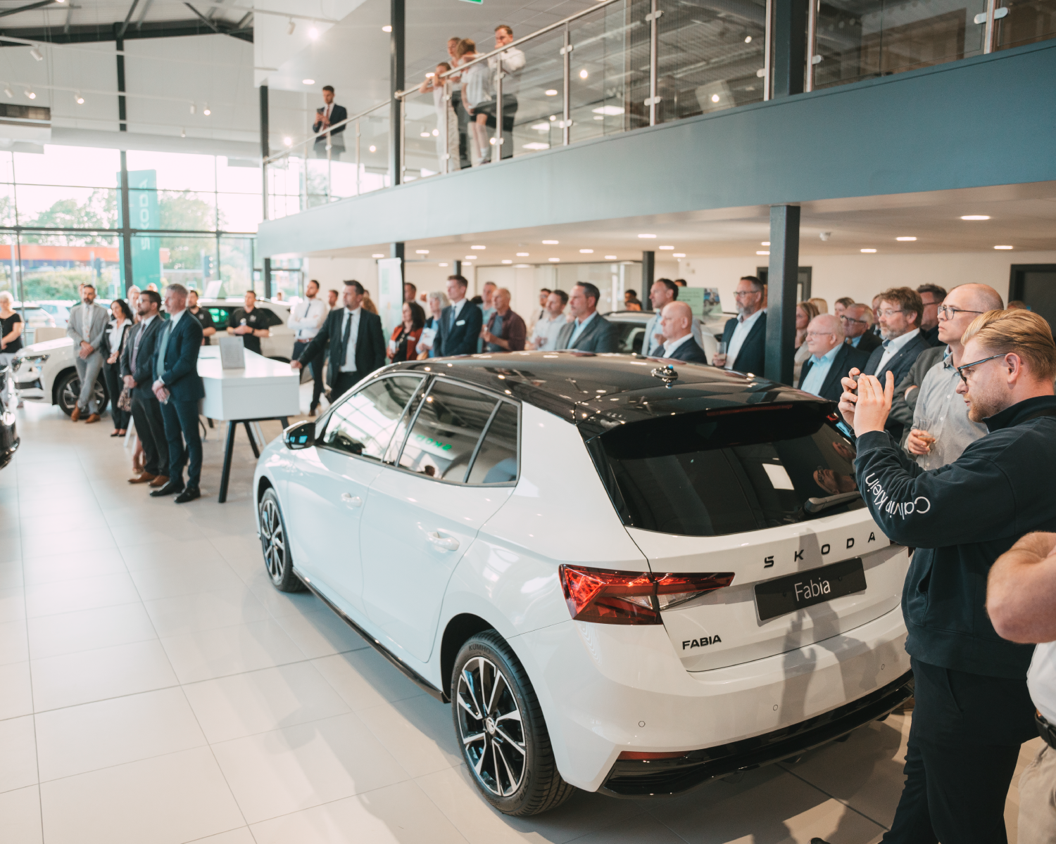 A sleek car showroom with people applauding its opening, with a white Skoda Fabia in the centre of the image