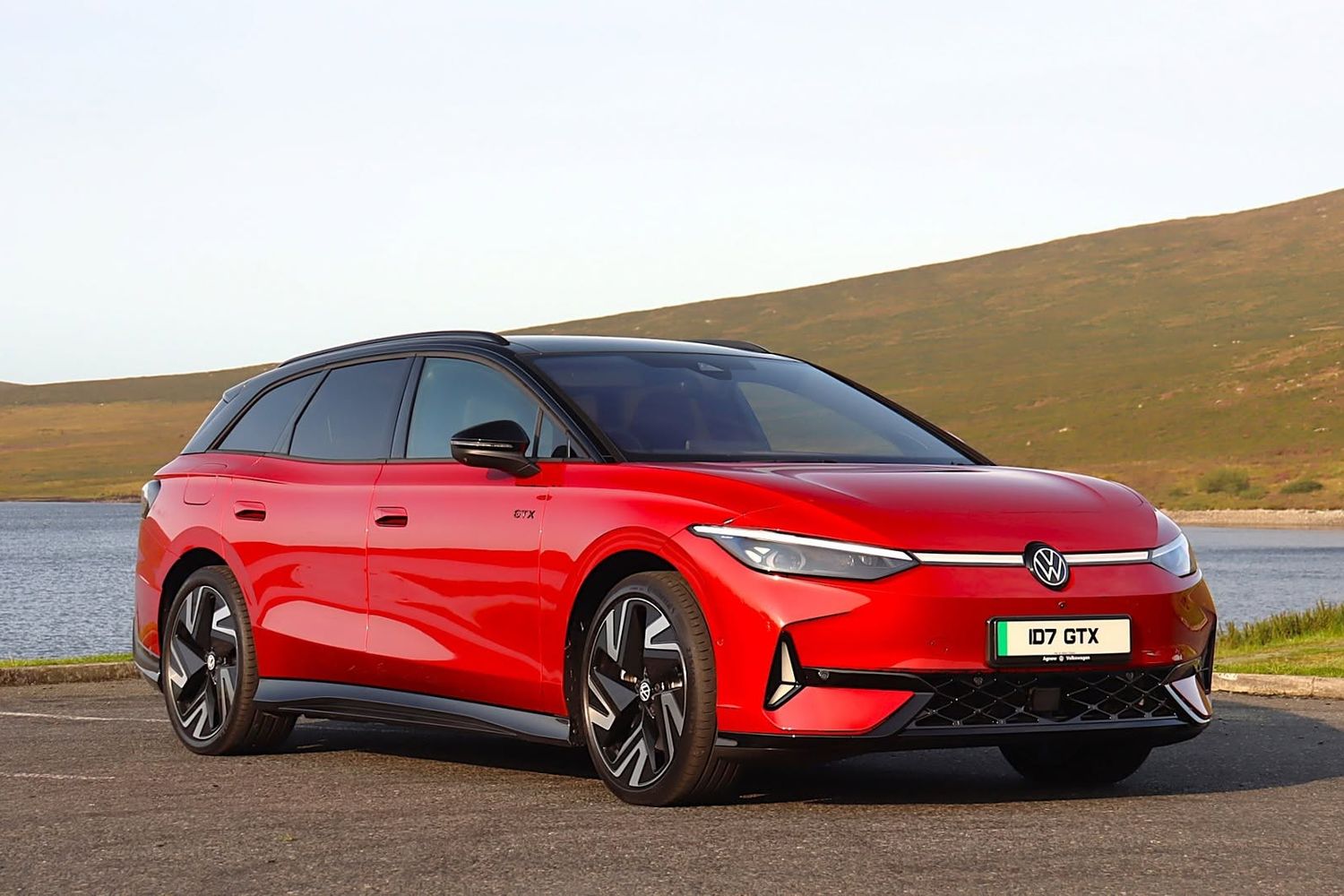 Front and side view of the new Volkswagen ID.7 in red, parked with a lake view behind