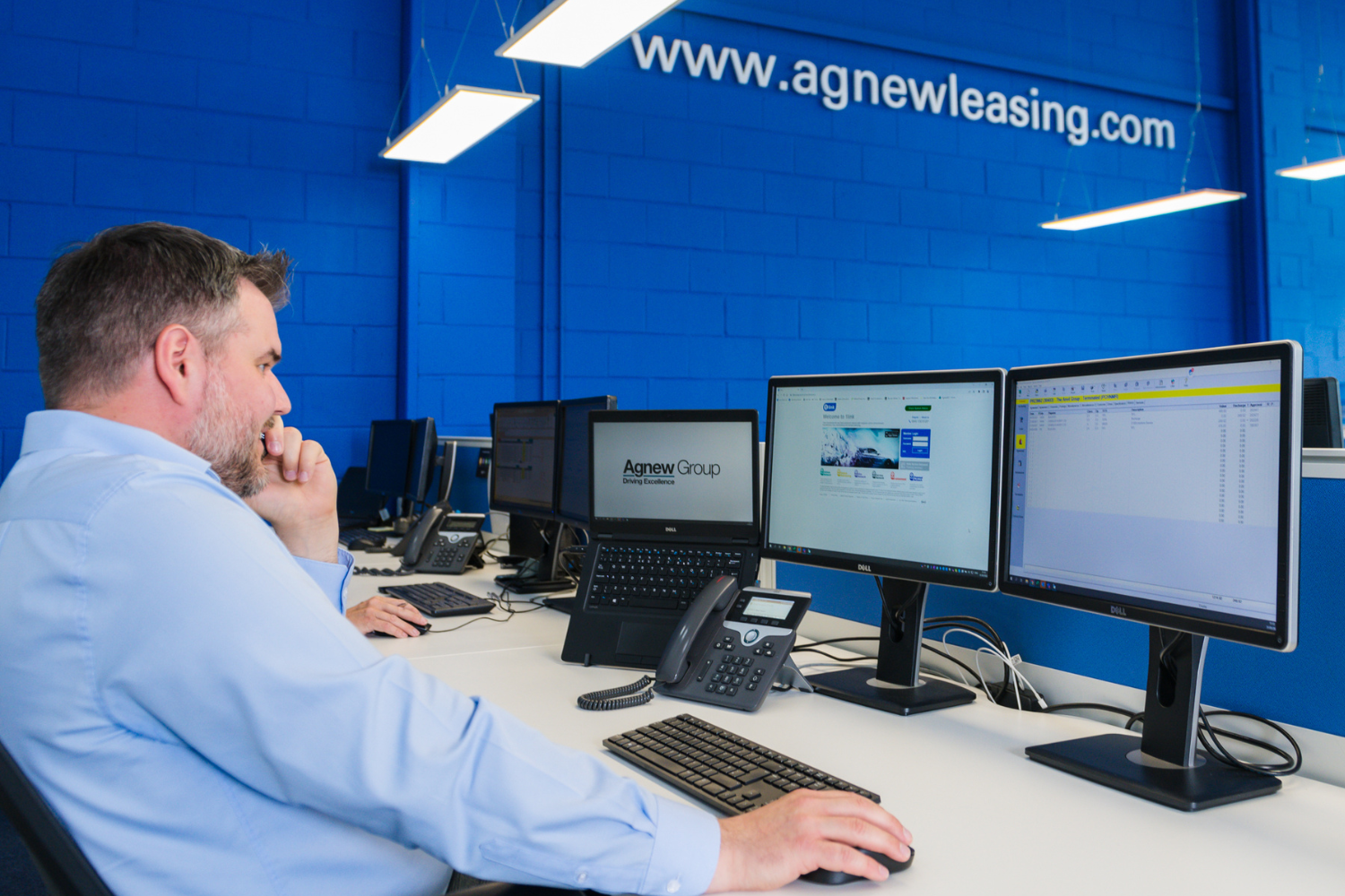 An Agnew Leasing employee talking on the phone to a customer as he looks at his work computer.