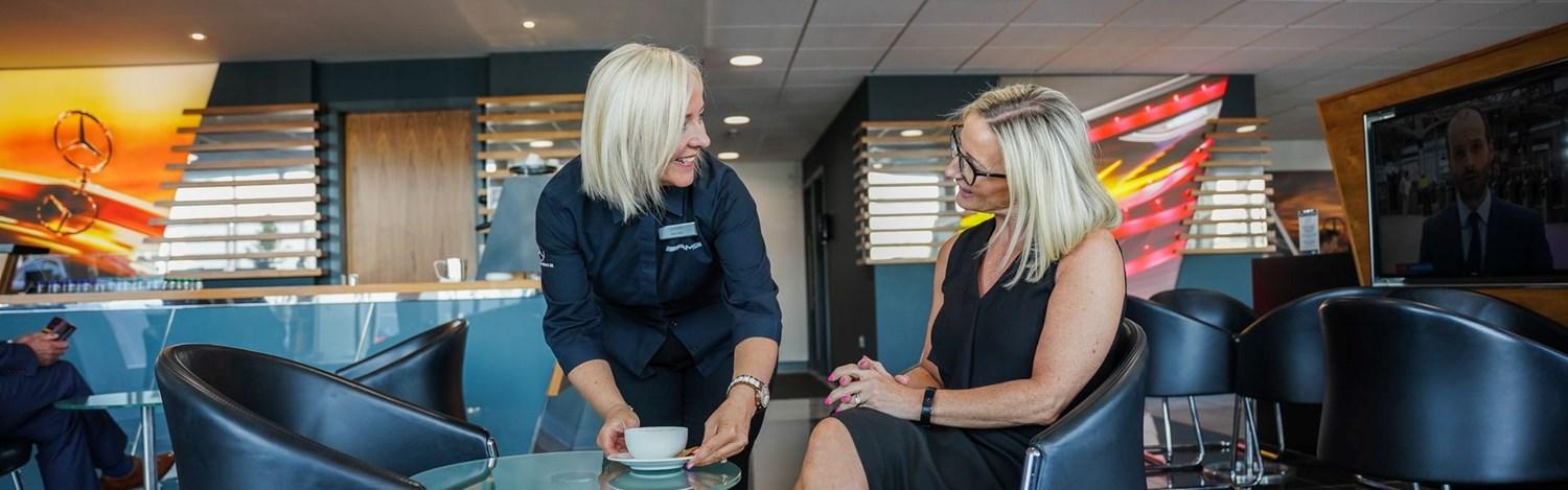 Mercedes-Benz Customer Service Specialist hands over coffee to customer who is waiting to find out more about Mercedes-Benz Warranties at the Mercedes-Benz of Belfast showroom