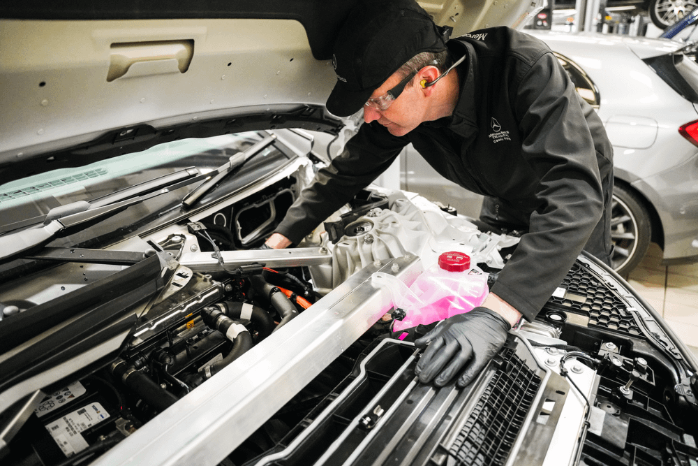 Mercedes-Benz Technician inspects under the hood of vehicle for repair during Premium Servicing work.