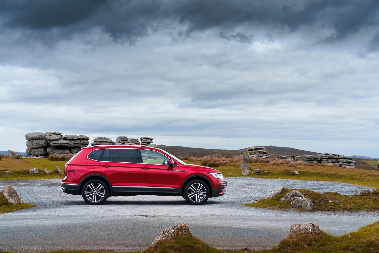 Side view of the new Volkswagen Tiguan Allspace in red, parked in car park with stone wall