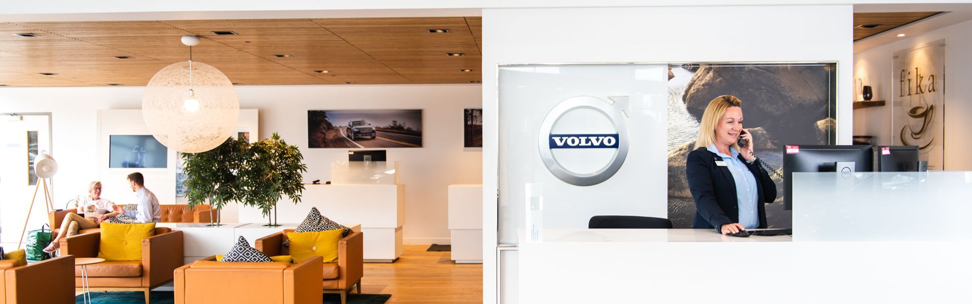 Two customers enjoy a cup of tea while they wait in the Agnew Belfast Volvo showroom as the Sales Specialist takes a call