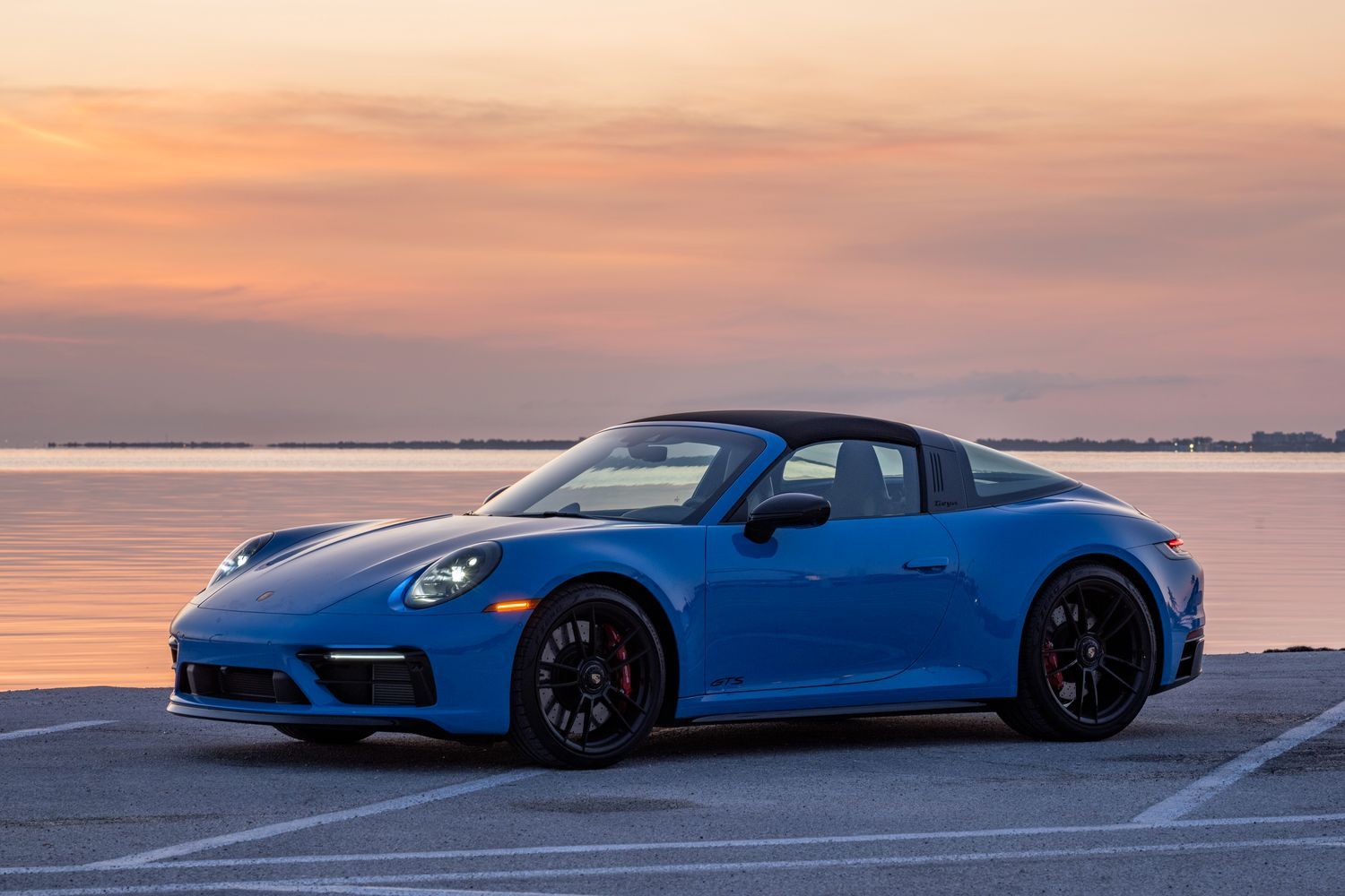 Side view of the all-new Porsche 911 Targa in blue, parked next to sea with sunsetting