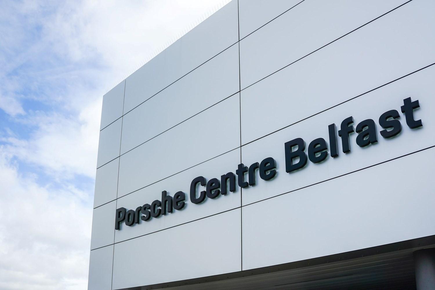 Exterior of the Porsche Centre Belfast showroom with 'Porsche Centre Belfast' sign on silver tiles.