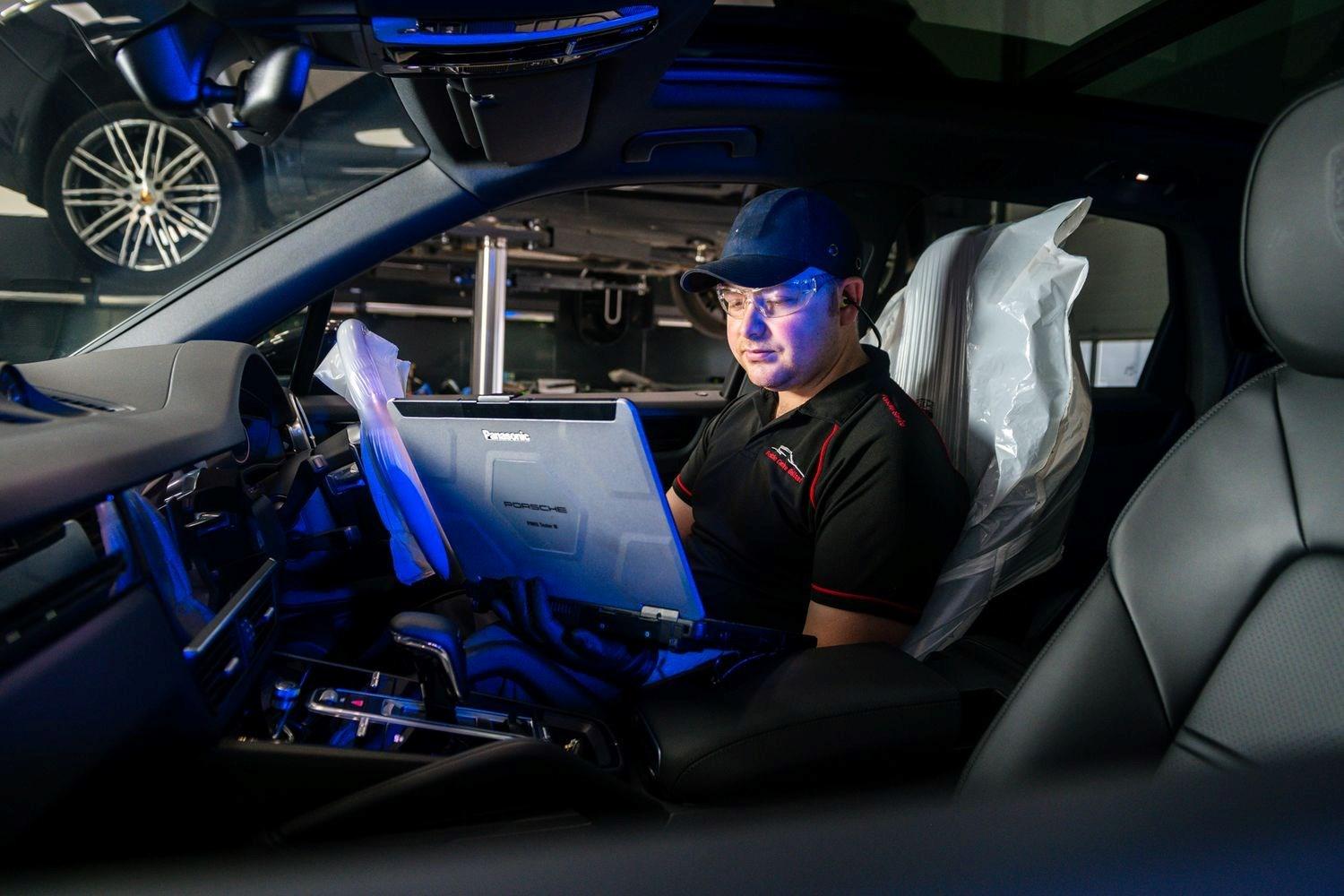 Porsche Centre Belfast Repair Specialist inspects the interior of a Porsche vehicle with laptop for internal electric maintenance and repairs at the Porsche Approved Repair Centre