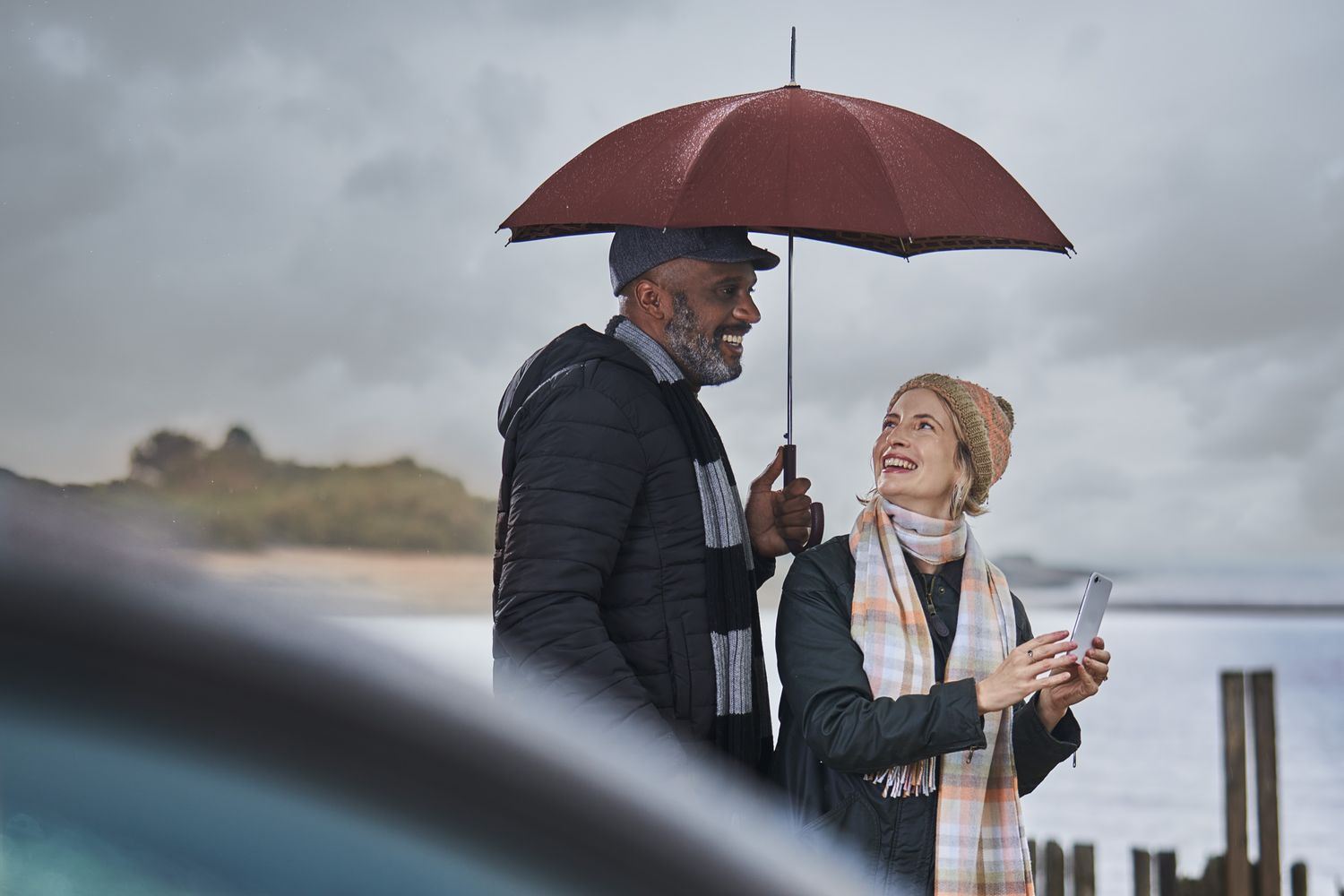 Man and woman at rainy beach beside car