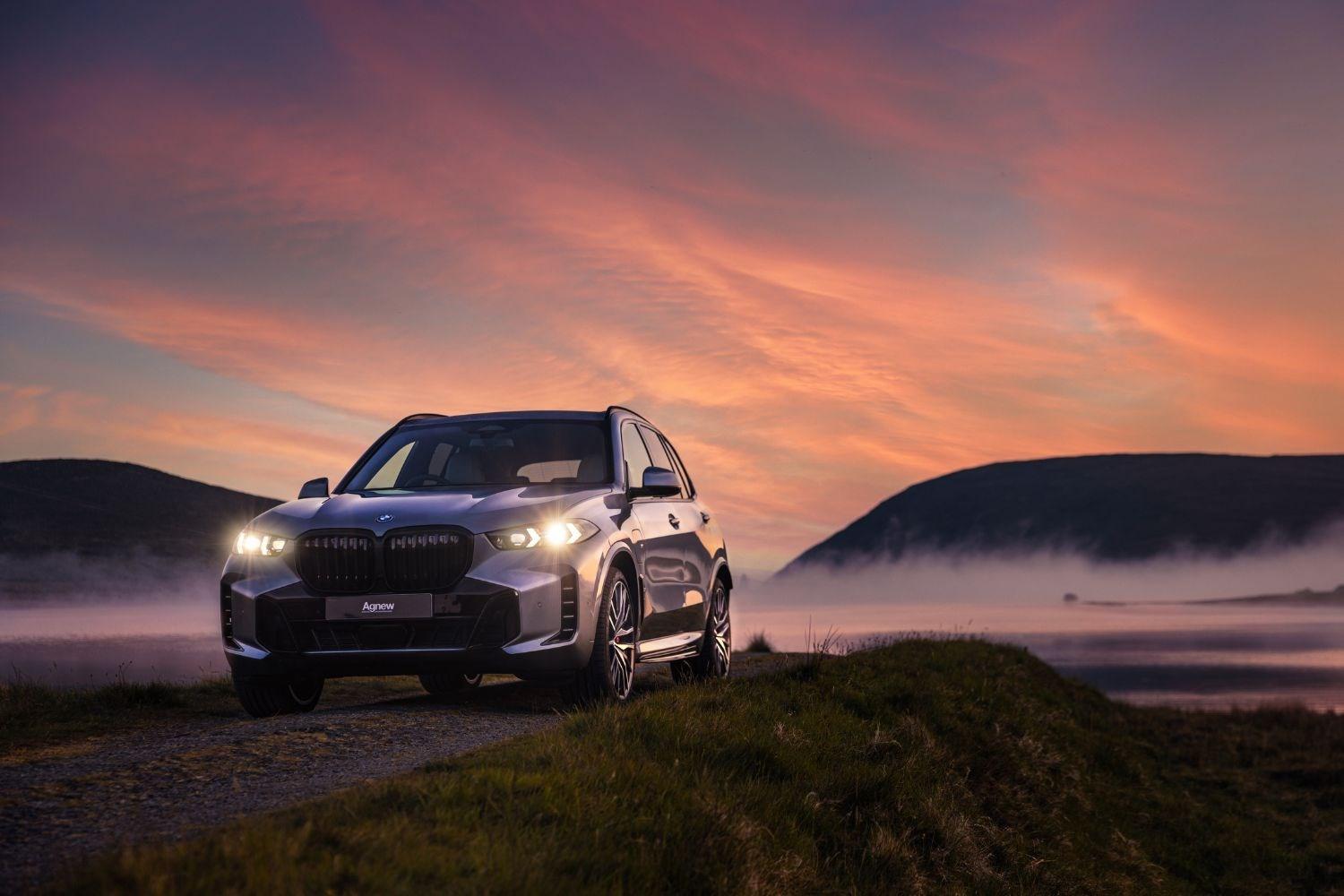 Front and side view of the latest BMW X4 parked by foggy lake at sunset