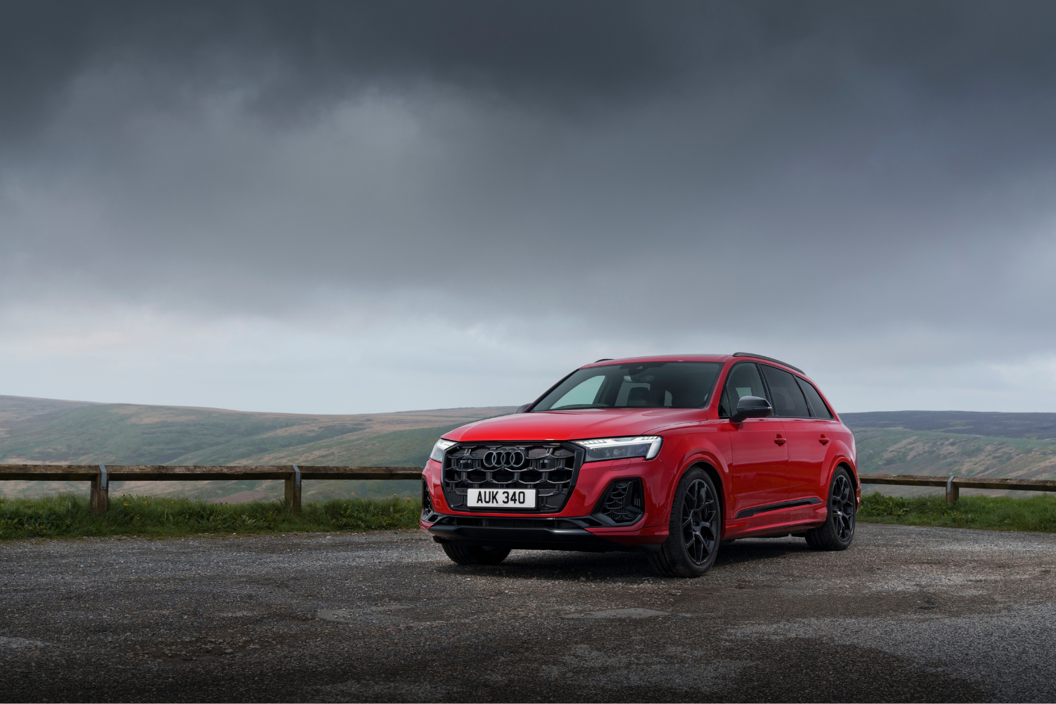 Latest Audi Q7 in red, parked in countryside background with grey skies behind