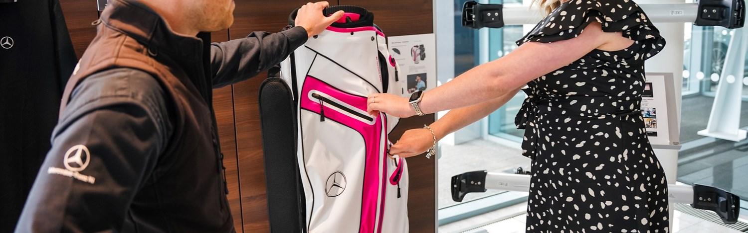 Mercedes-Benz customer service specialist and customer look at white and red Mercedes-Benz golf bag