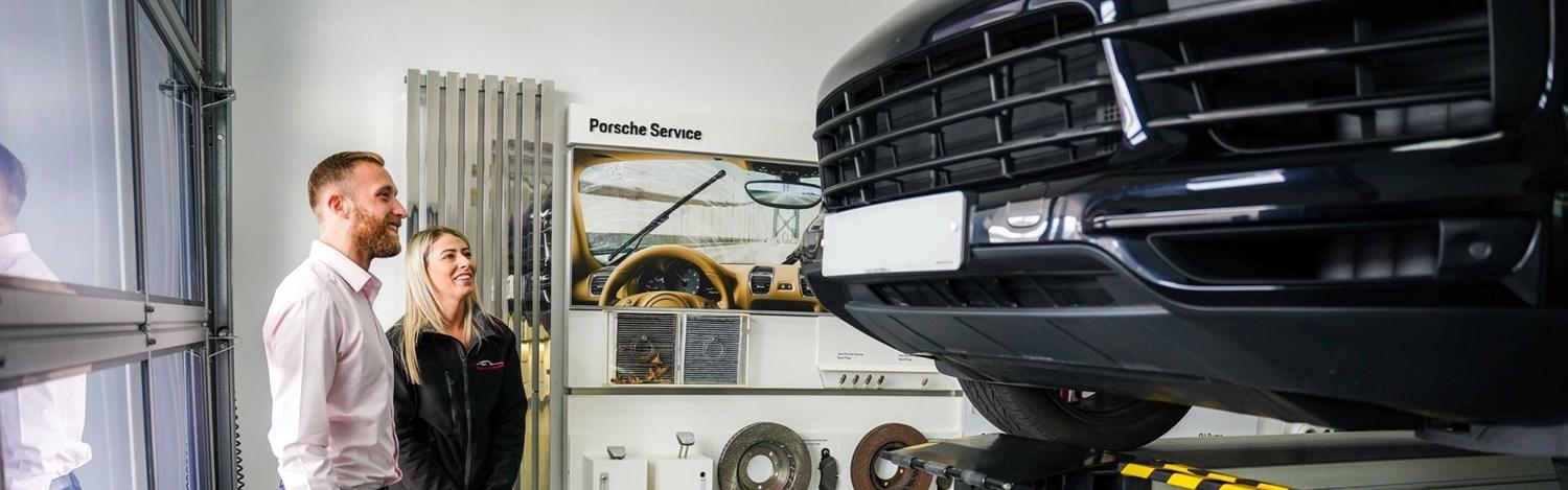 Porsche Centre Belfast Repair Specialist discusses the repairs that will be made to the customers Porsche vehicle as their Porsche Cayenne is on a car lift.