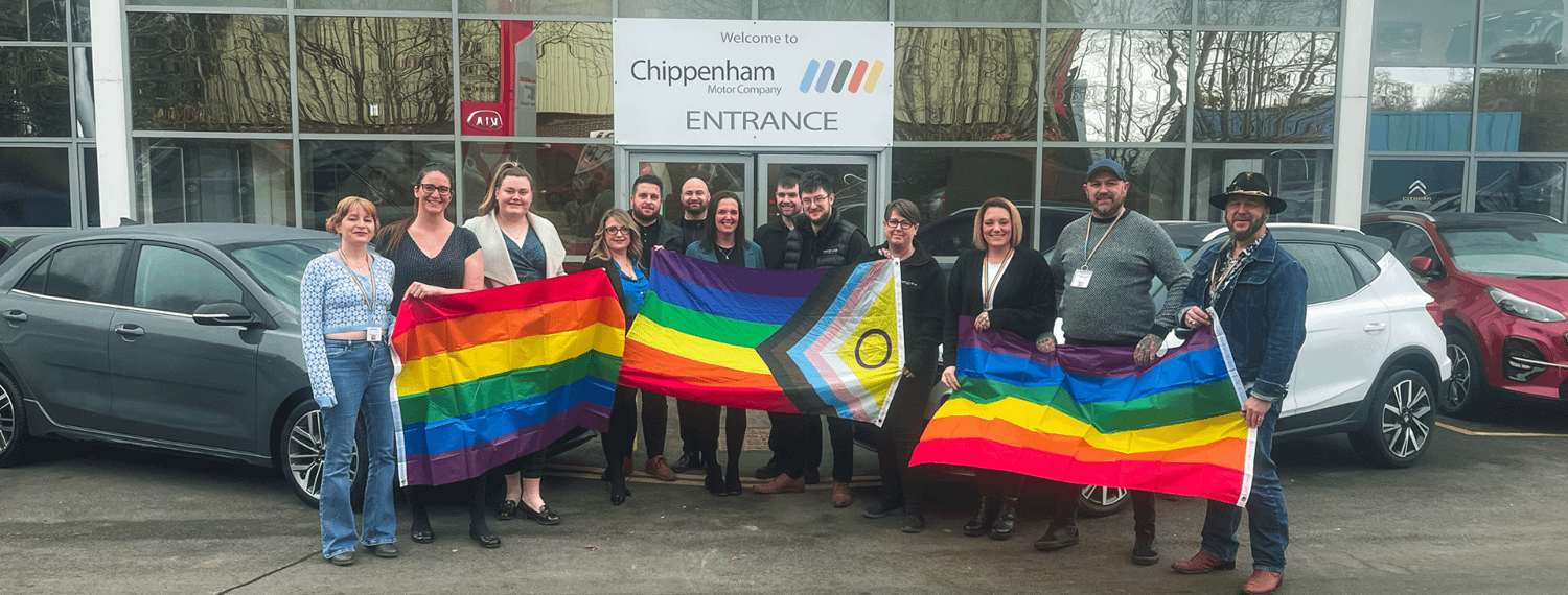 Chippenham Motor Company and Chippenham Pride 2023 teams outside of the car dealership holding PRIDE flags