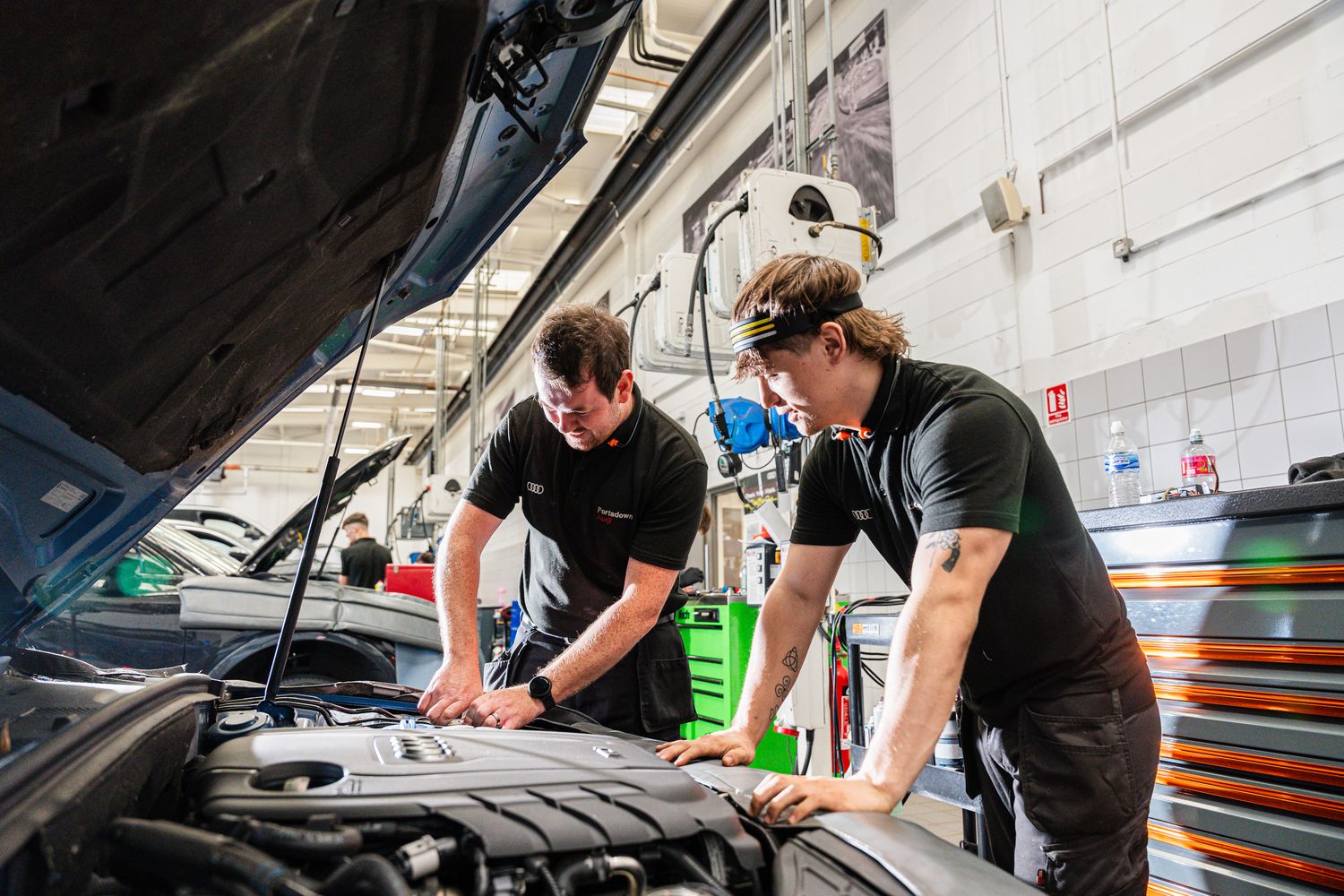 Two Audi Technicians inspect inside the hood of an Audi
