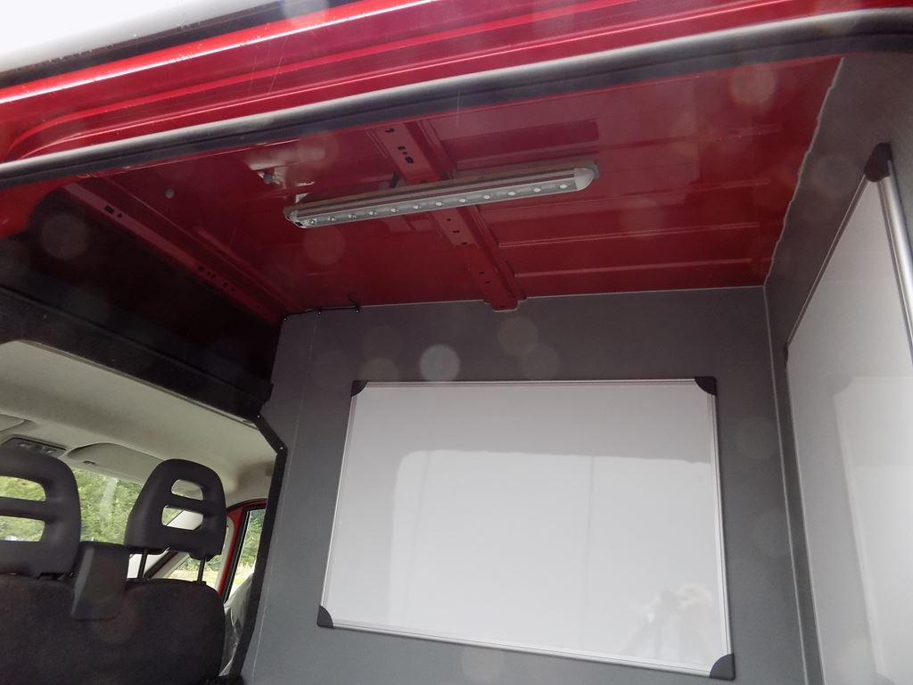 Van interior workspace with wall-mounted whiteboard and overhead LED light.