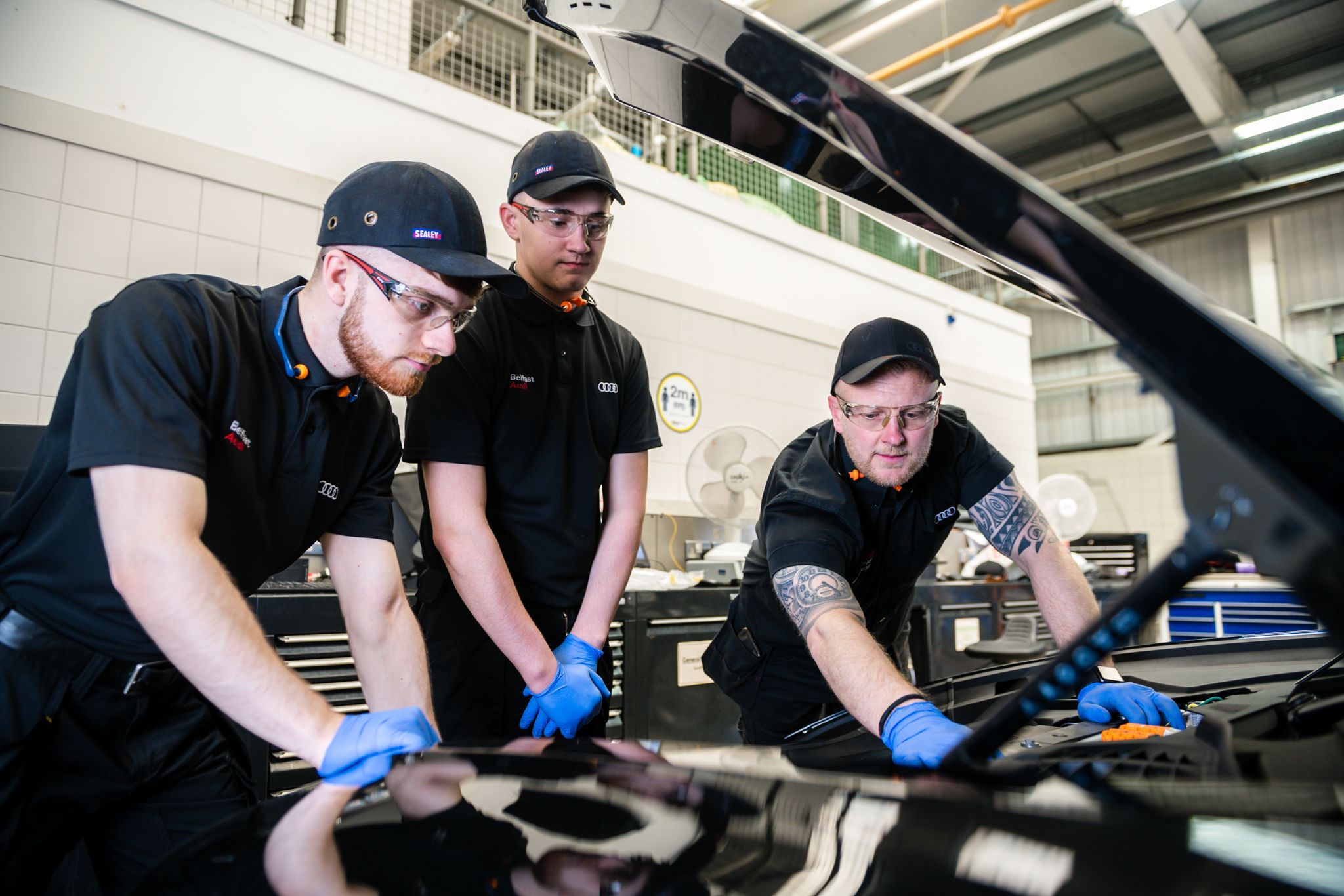 Three Audi technicians inspect under the hood of Audi vehicle