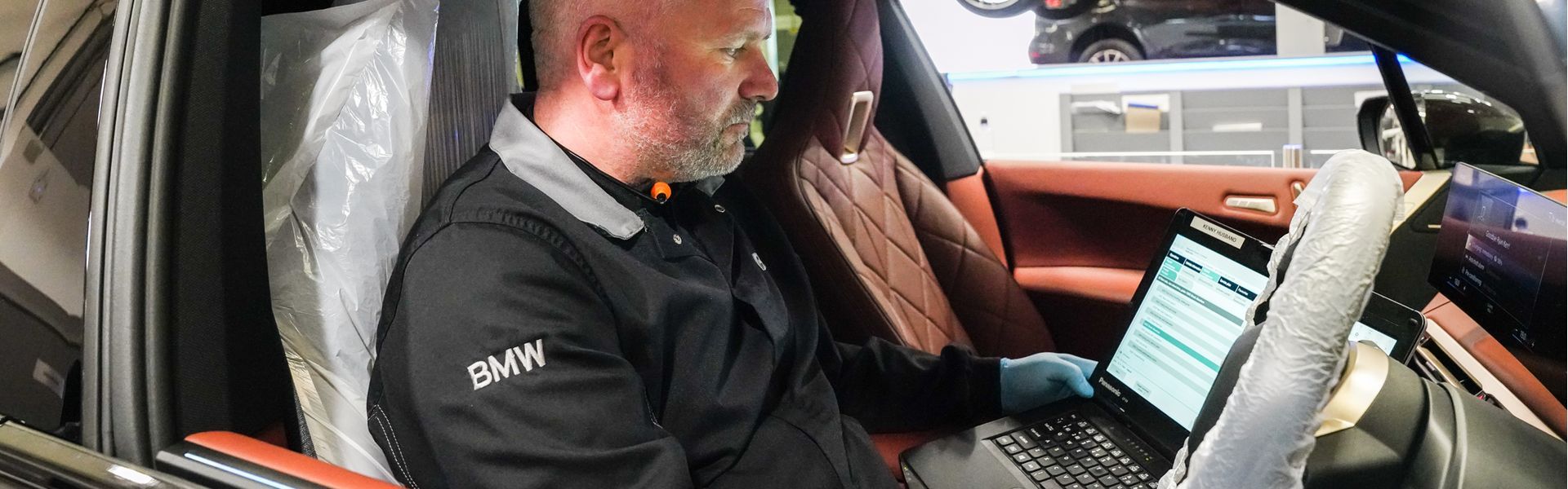 BMW Technician sits in driver seat and checks for electrical issues on laptop during vehicle repair at Bavarian BMW Belfast