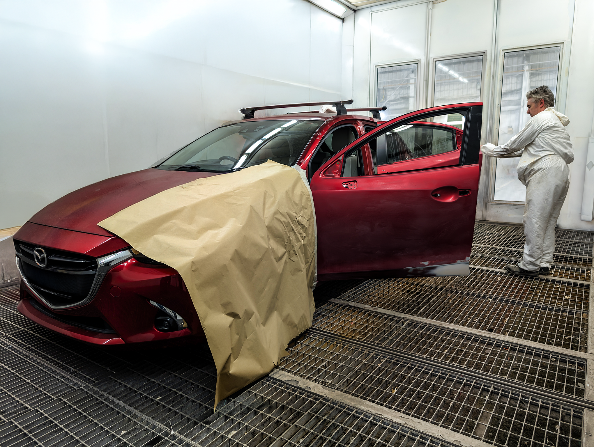 Technician standing next to a red vehicle in a spray painting booth