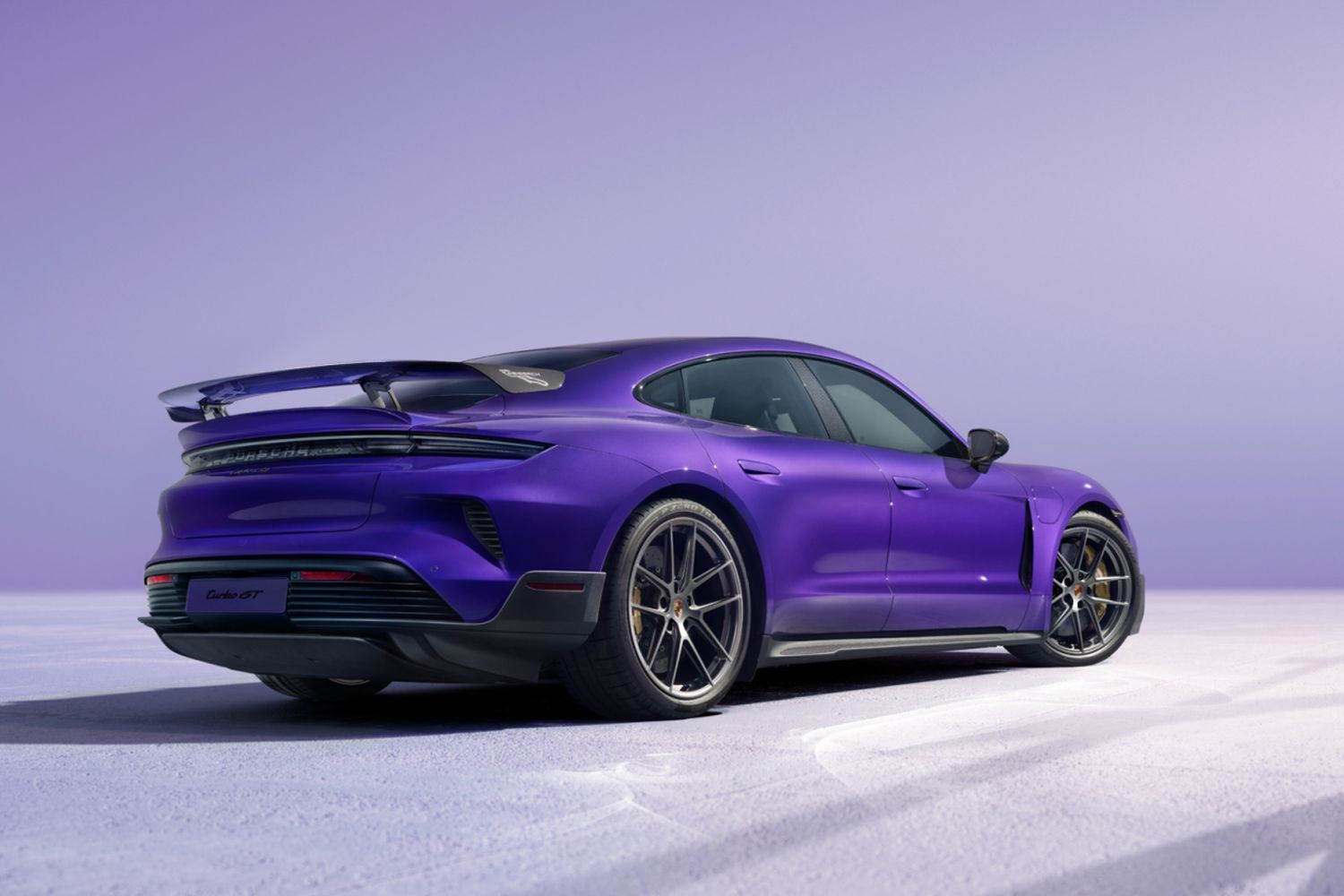 Rear and side view of the Porsche Taycan Turbo GT (in purple) with Weissach Package at night, on neutral background.