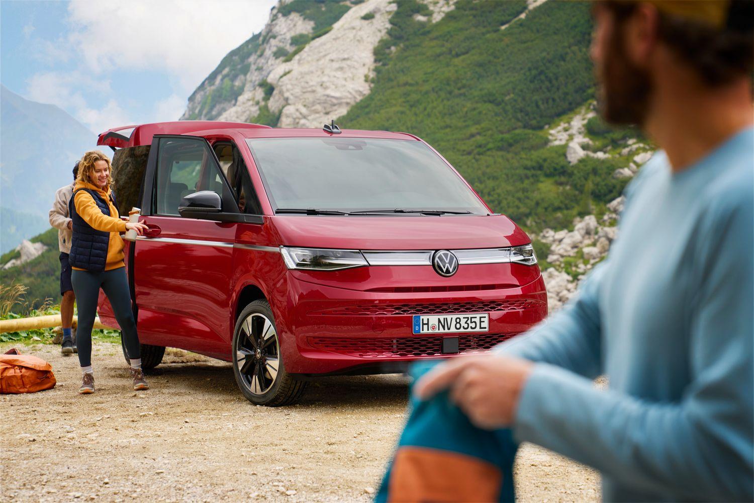 Front view of the Volkswagen Multivan. Woman packs away camping gear using the front and rear entrances.